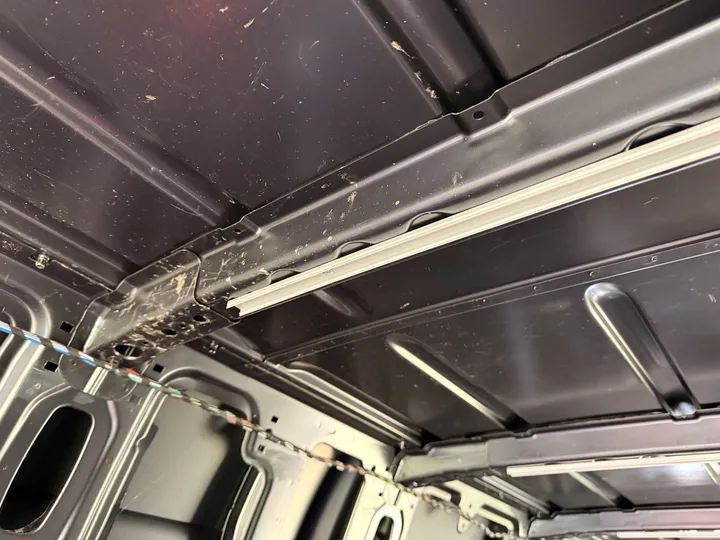 Up at the roof: the aluminium LED strip housing riveted along a rib, with one loom wire still looped across the corner.