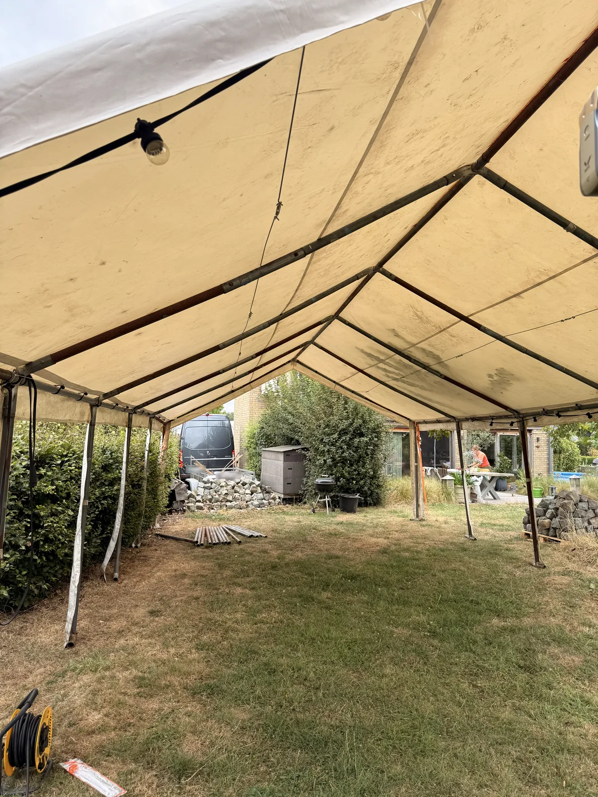 Inside the beige marquee on the dried out lawn, with the grey Sprinter parked behind the hedge