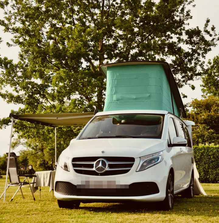 The white Marco Polo on a campsite, roof up and awning out