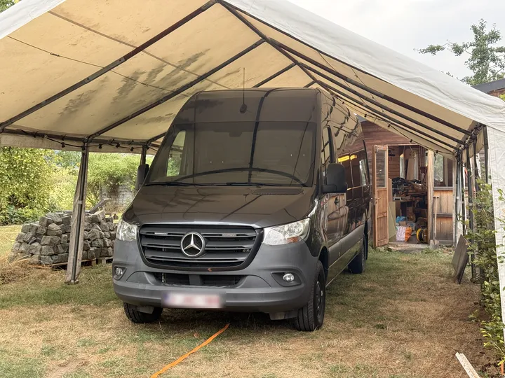 The grey Sprinter parked nose first under the beige marquee, with the workshop shed behind it